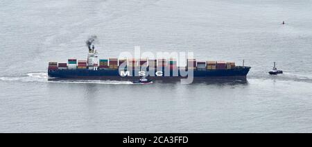 Ein Containerschiff, das von zwei Schleppern in der Mündung des Flusses Mersey, Liverpool Port, Großbritannien, manouvered wird Stockfoto