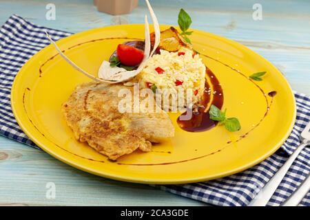 Gebratenes Fischfilet Tilapia und Reis mit Gemüse und Sauce auf einem gelben Teller. Nahaufnahme Essen auf dem Tisch. Fischmenü mit Mikrogrün im Stockfoto