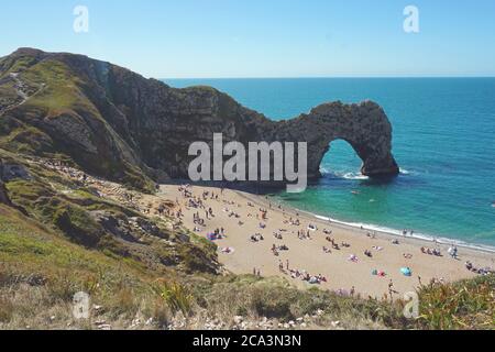 Sonnenanbeter genießen die Sonne und den Blick auf Durdle Door mit seinen Sandstränden und dem ikonischen Kalksteinbogen, Lulworth Estate, Dorset, Großbritannien Stockfoto