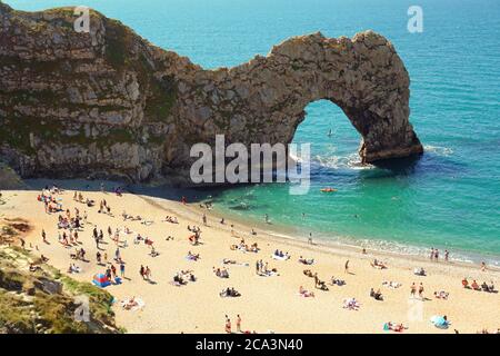 Sonnenanbeter genießen die Sonne und den Blick auf Durdle Door mit seinen Sandstränden und dem ikonischen Kalksteinbogen, Lulworth Estate, Dorset, Großbritannien Stockfoto