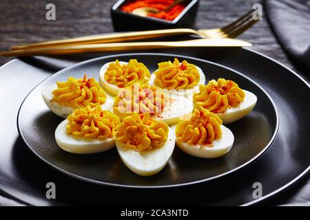 Einfache, deviled Eier aus zertrümmerten Eigelb Senf, Mayonnaise, Essig mit geräuchertem Paprika auf einem schwarzen Teller auf einem dunklen Holzgrund bestreut Stockfoto