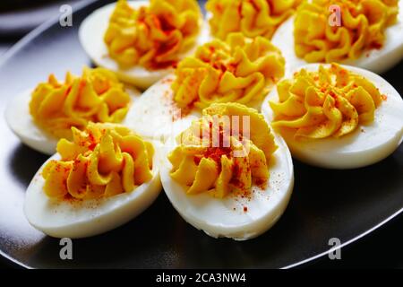 Nahaufnahme von cremigen, deviled Eiern von zertrümmerten Eigelb, dijon-Senf, Mayonnaise, Weißessig mit geräuchertem Paprika auf einem schwarzen Teller mit Gol bestreut Stockfoto