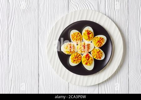 American Deviled Eier zerschlagen Eigelb, dijon-Senf, Mayonnaise, Apfelessig bestreut mit geräuchertem Paprika auf einem schwarzen Teller auf einem weißen w Stockfoto