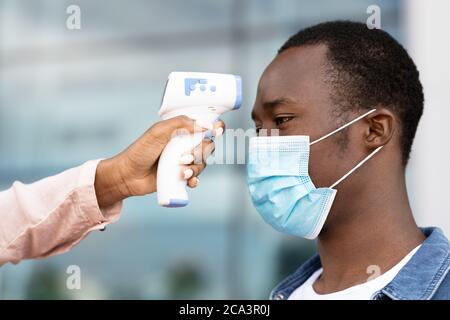 Sicherheitsprüfung Der Körpertemperatur Mit Elektronischem Thermometer Für Black Man Im Flughafen Stockfoto