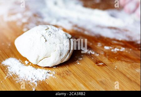 Ein frischer Teig auf einem bemehlten Holzbrett. Zubereitung und Zutaten für Pizza, Brot und Pasta. Rohkost Stockfoto