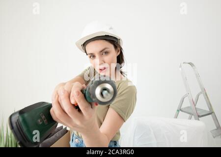Portrait von selbstbewussten jungen Frau in Hardhat mit Power-Schraubendreher während der Renovierung in neue Wohnung Stockfoto