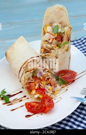 Burrito auf einem weißen Teller in einem Restaurant. Eine schnelle Mahlzeit mit gebratenem Huhn, Sauce, rote Zwiebeln, Mais, Tomaten. Burritos Wraps mit Rindfleisch und Gemüse. A Stockfoto