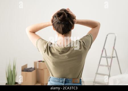 Rückansicht der Brünette Frau hält Kopf in den Händen, während das Gefühl Kopfschmerzen von der Festsetzung Dinge in der Wohnung Stockfoto