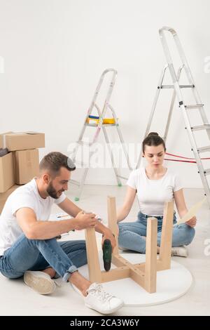 Junges Paar Umzug in neues Haus sitzen auf dem Boden und Montage Couchtisch zusammen Stockfoto