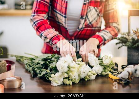 Sorgfältige attraktive junge Frau arbeiten als Floristin, genießen Sie die Arbeit mit Botanik rund um Pflanzen und Blumen. Kleinunternehmerbesitzer machen Strauß Stockfoto