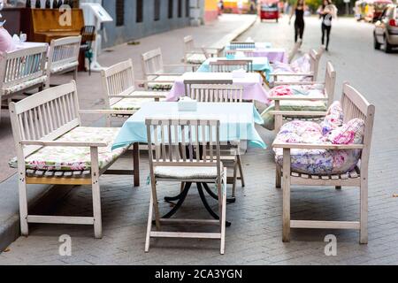 Café im Freien mit Holztischen und Bänken mit weichen Kissen und Tischdecken auf einer Fußgängerstraße mit Pflasterplatten bedeckt. Stockfoto