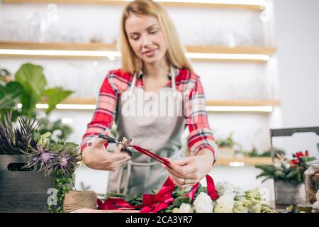 Junge kaukasische Dame mit blonden Haaren gerne als Floristin arbeiten, attraktive Besitzer des Geschäfts, junge Gärtner rund um Pflanzen kümmern sich um Blumen Stockfoto