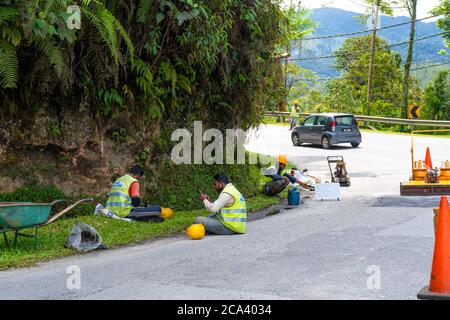 Straßenreparatur in Asien. Eingezäunter Straßenabschnitt mit Grube. Arbeiter in Overalls ruhen am Rande, Mittagspause Stockfoto