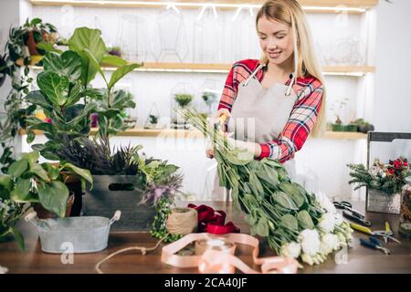 Charming schöne glückliche junge Floristin Frau im Gewächshaus voller Blumen und Pflanzen stehen, genießen Sie die Arbeit mit Botanik Stockfoto