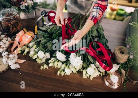 Cropped sorgfältige Floristen machen, komponieren Strauß von weißen schönen Rosen für Kunden in ihrem eigenen Shop, rotes Band auf Blumen. Pflanzen, Blumen, Dekor Stockfoto