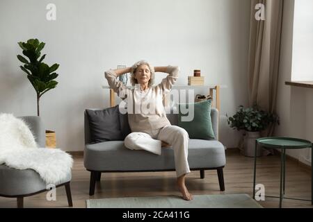 Im Wohnzimmer auf moderne bequeme Couch entspannend reife Frau Stockfoto