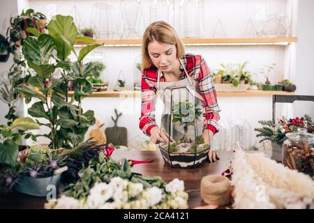 Junge und schöne kaukasische Liebhaber von Pflanzen und Blumen kümmern sich um Pflanzen, blonde Dame von Botanik umgeben, grüne Pflanzen in Töpfen Stockfoto