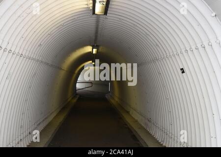 Städtische Fußgängerunterführung oder Unterführung unterhalb der Autobahn. Passage hat gewellte Oberfläche der Wände in Form von weißen Tunnel mit Deckenleuchten. Stockfoto