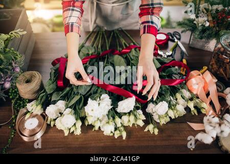 Draufsicht auf Cropped sorgfältige Floristen machen, Komposition Bouquet von weißen schönen Rosen für Kunden in ihrem eigenen Shop, rotes Band auf Blumen. Pflanzen, fl Stockfoto