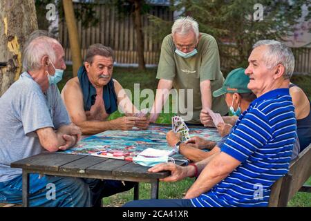 Zrenjanin, Serbien, 29. Juli 2020. Ältere Herren und Rentner spielen jeden Tag Karten im Schatten eines großen Baumes. Es gibt immer neugierige Beobachter Stockfoto