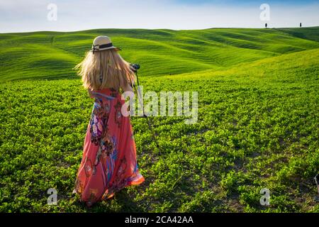 Orcia Valley, Siena Bezirk, Toskana, Italien, Europa. Blonde Frau mit Hut macht Bilder in grünen Feldern. Stockfoto