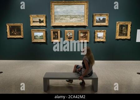 London, Großbritannien. August 2020. Ein Mitarbeiter posiert mit Werken von Delacroix und Corot in einer Nachbildung einer Ausstellung in Ordrupgaard. Vorschau auf 'Gauguin und die Impressionisten : Meisterwerke aus der Ordrupgaard Collection' an der Royal Academy of Arts in Piccadilly. 60 Werke aus einer Sammlung impressionistischer Gemälde des wohlhabenden dänischen Ehepaars Wilhelm und Henny Hansen, die vom 7. August bis zum 18. Oktober 2020 ausgestellt werden, sind Meisterwerke von Gauguin, Degas, Monet, Morisot, Pissarro, Renoir und Sisley. Kredit: Stephen Chung / Alamy Live Nachrichten Stockfoto