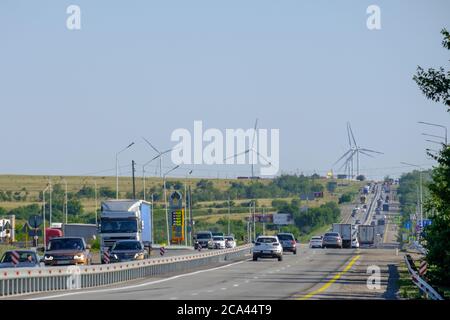 Juli 25, 2020. Region Rostow. Russland. Autoverkehr auf der Autobahn mit Windturbinen am Horizont. Eine alternative Quelle sauberer Windenergie. Heiß Stockfoto