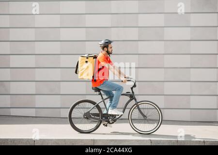 Kurier Radfahrer auf grauen Wand Hintergrund. Junger Mann im Helm mit Rucksack fährt auf der Straße Stockfoto