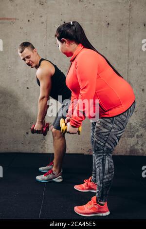Übergewichtige Frau mit persönlichen Fitness-Trainer tun Übung mit Hanteln.Frau hat Probleme mit der Gesundheit.Seitenansicht voller Länge Foto Stockfoto