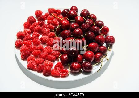 Mischung aus Kirschen und Himbeeren auf Teller isoliert auf weißem Hintergrund. Sommer, vegetarisches Konzept Stockfoto