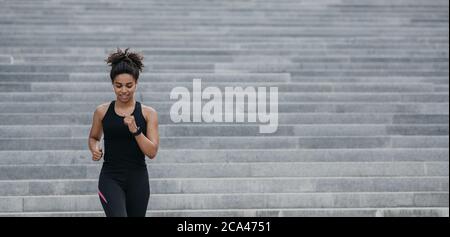 Starke sportliche Frau läuft. Glückliches Mädchen in Sportbekleidung mit Fitness-Tracker tun Cardio-Training auf Treppen Stockfoto