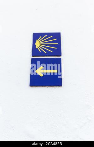 Camino de Santiago Gelbes Jakobsmuschel- und Pfeilschild an weißer Wand. Jakobsweg Zeichen Pilgerfahrt nach Santiago de Compostela. Speicherplatz kopieren Stockfoto