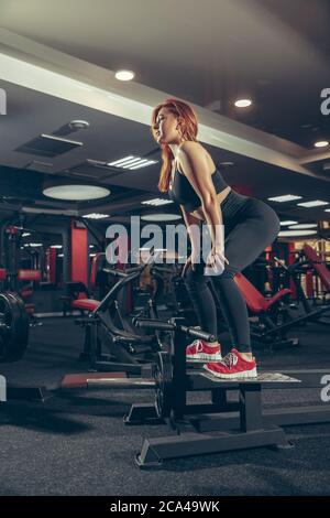 Schwer. Junge muskulöse kaukasische Frau, die im Fitnessstudio mit Geräten praktiziert. Sportliche weibliche Modell macht Übungen, Training ihren Oberkörper, Training mit Ball. Wellness, gesunder Lebensstil, Bodybuilding. Stockfoto