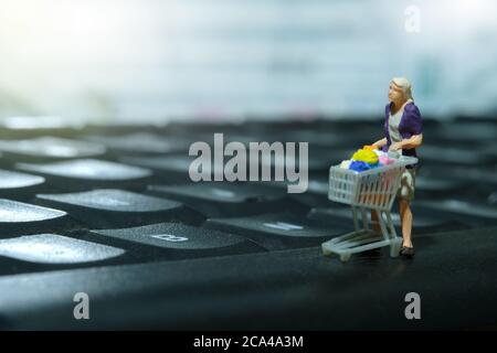 Eine Frau, die Online-Shopping macht. Gehen mit Warenkorb Shop über Tastatur. Miniatur Menschen Figuren Spielzeug konzeptionelle Fotografie. Stockfoto