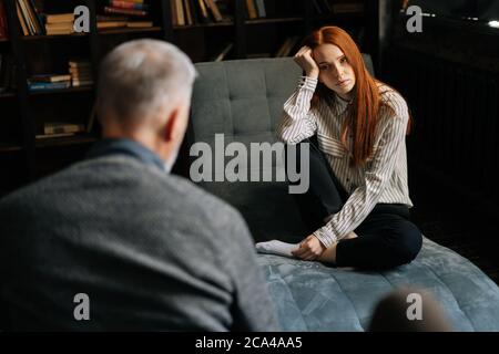 Frustrierte junge rothaarige Dame in Freizeitkleidung hat Therapiesitzung mit Psychologe. Stockfoto