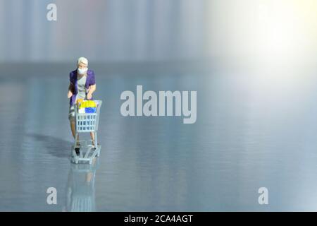 Eine Frau, die im Supermarkt sicher einkauft und eine Gesichtsmaske trägt. Miniatur Menschen Figuren Spielzeug konzeptionelle Fotografie. Stockfoto