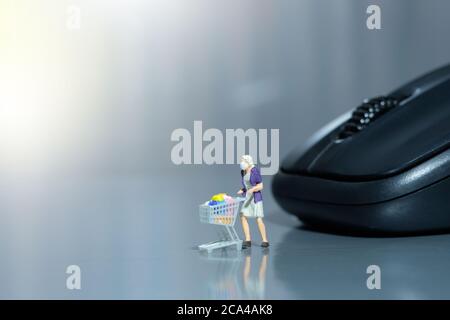 Online-Shopping. Frauen mit Wagen vor schwarzer Maus. Miniatur Menschen Figuren Spielzeug konzeptionelle Fotografie. Stockfoto