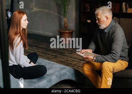 Seitenansicht der rothaarigen jungen Patientin, die mit einem reifen Psychologen spricht. Stockfoto