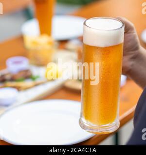 Mann hält Bierkrug mit Snacks auf dem Tisch Stockfoto