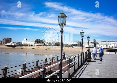 Blick auf die Küste vom Worthing Pier mit dem großen Rad unter blauem Himmel und Menschen genießen den Sommer am Strand während der Sperre in Worthing, West Sussex Stockfoto