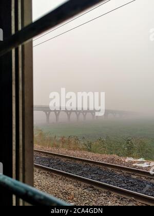 Ein Schuss aus dem Inneren eines Zuges. Ein Blick auf eine im Nebel gehüllte Brücke, Delhi Indien. Stockfoto