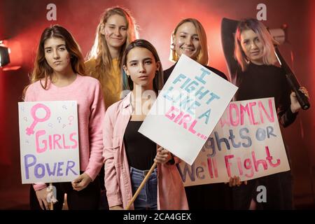 Junge kurzhaarige feministische Frauen mit großen Plakaten, die für Feminismus kämpfen, stylische und trendige Feministinnen-Mädchen im rauchigen Raum Stockfoto