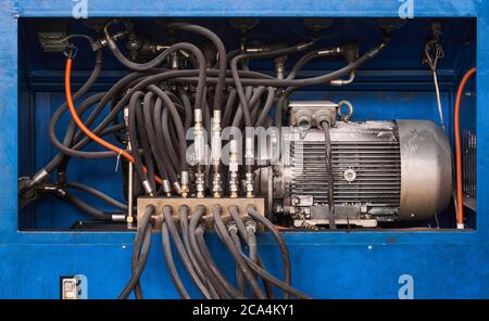 Industrieller Hintergrund - Elektromotor, Pumpe und Regelventile mit Schläuchen einer hydraulischen Maschine aus der Nähe Stockfoto