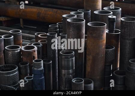 Industrieller Hintergrund - rostige Beschläge, Teile von Turbobohrern mit verschiedenen Durchmessern sind auf dem Boden in einer halbdunklen Werkstatt Stockfoto