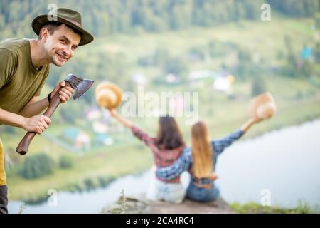Schlauer lächelnder Mörder, der zwei Schwestern töten wird, die am Rand sitzen, oben auf dem Berg, verschwommener Hintergrund, erstaunliche Landschaft im Hintergrund Stockfoto