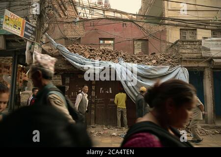 Fußgänger gehen auf einer Straße vor einem Gebäude, das von den Erdbeben in Nepal 2015 in Thamel, Kathmandu, Nepal zerstört wurde. Stockfoto