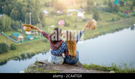 Lustige attraktive Mädchen mit gestreckten Armen Holsing Hüte Spaß beim Ausruhen auf der Oberseite des Felsens. Rückansicht close up Foto Stockfoto