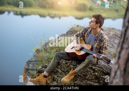 Talentierter kreativer Mann spielt Gitarre auf dem Berg, auf der Suche nach der Inspiration, genießen Sie die snset, Seitenansicht Foto.copy Raum, Hobby, Lifestyle, Stockfoto