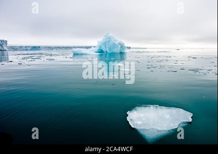 Ein Weitwinkel-Ansicht von schmelzenden Meereisschollen in stillen Gewässern der nördlichen Arktis mit Eisberg und Gletscherwand im Hintergrund.Klimakrise und Bruch Stockfoto