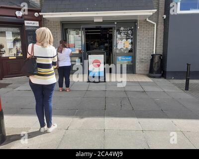 Schlange von Menschen außerhalb zeigen auf Höhe der Beschränkungen warten Zum Kauf von Waren und Einkaufen Covid 19 Coronavirus Soziale Distanzierung Stockfoto